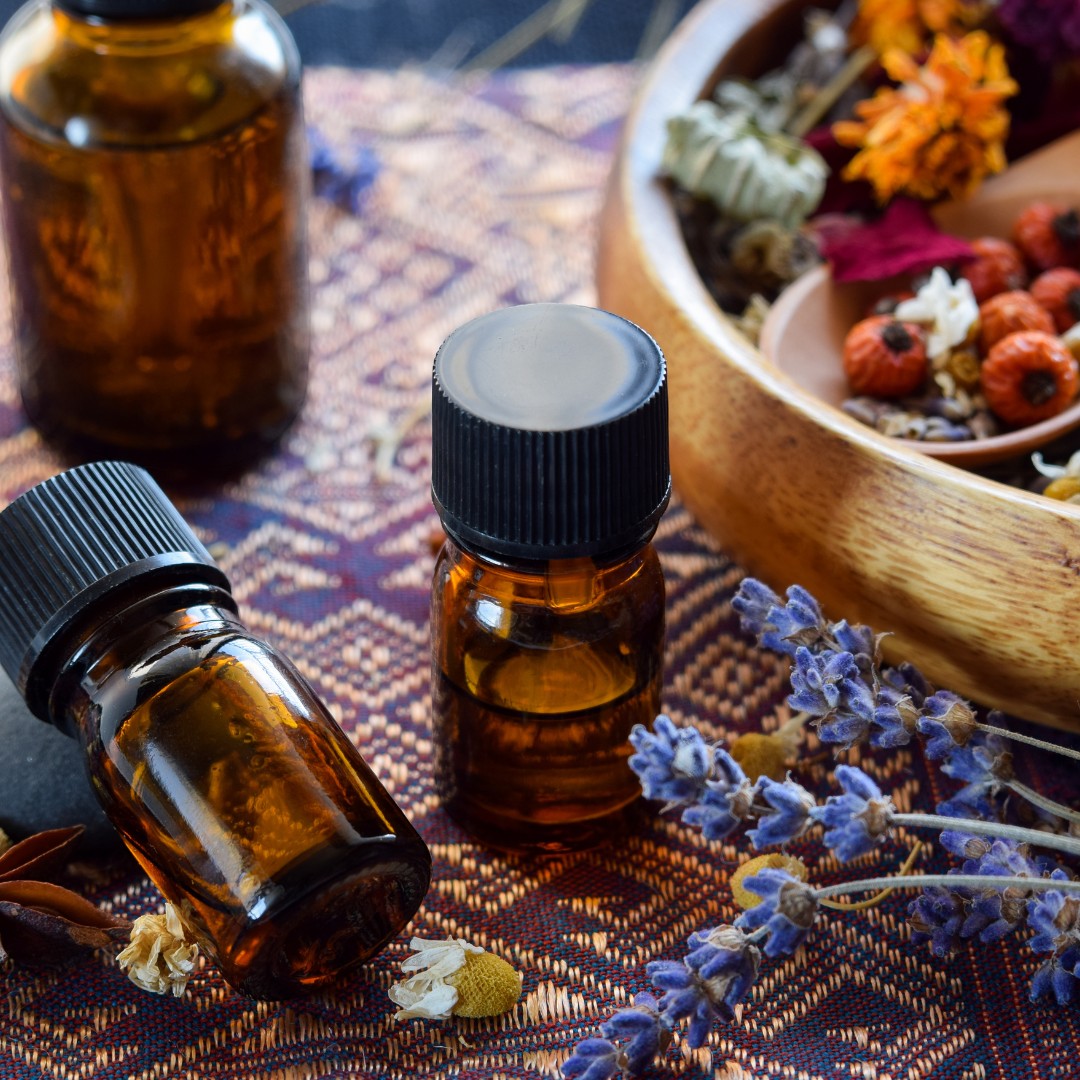 JoyfulBliss Co. Defense Ritual Anointing Oil in amber glass bottles with dried lavender and herbs on a patterned cloth.