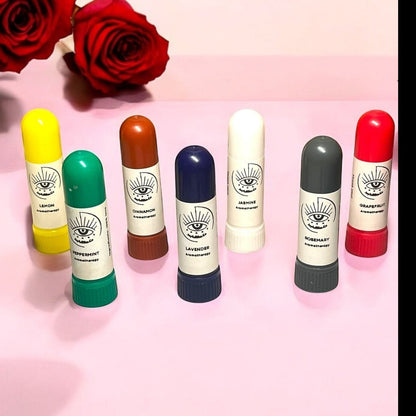 JoyfulBliss Co. set of seven colourful aromatherapy essential oil inhalers with eye logo on a pink surface with roses.