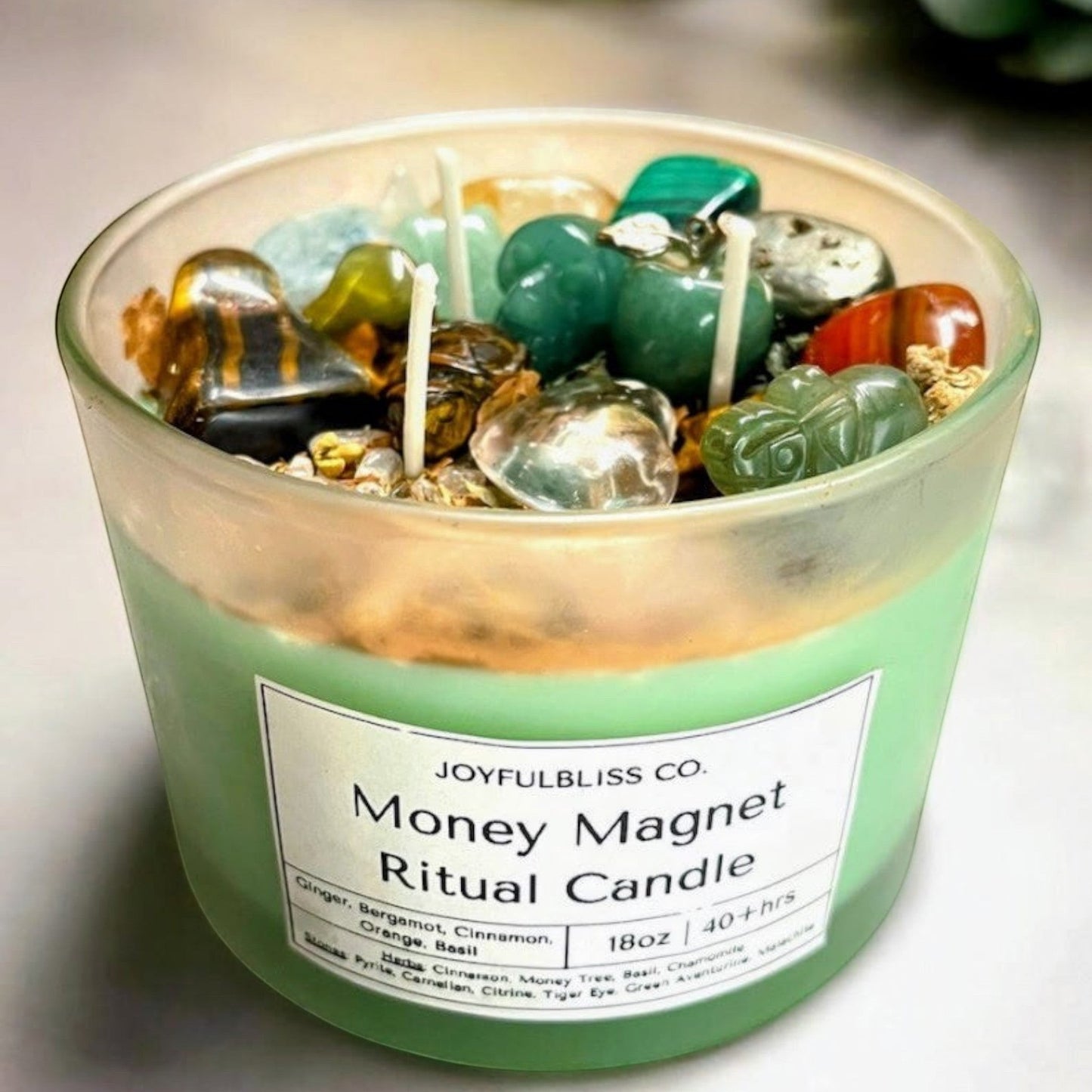 JoyfulBliss Co. Money Magnet ritual candle in a frosted glass jar with crystals, botanicals, and triple cotton wicks.