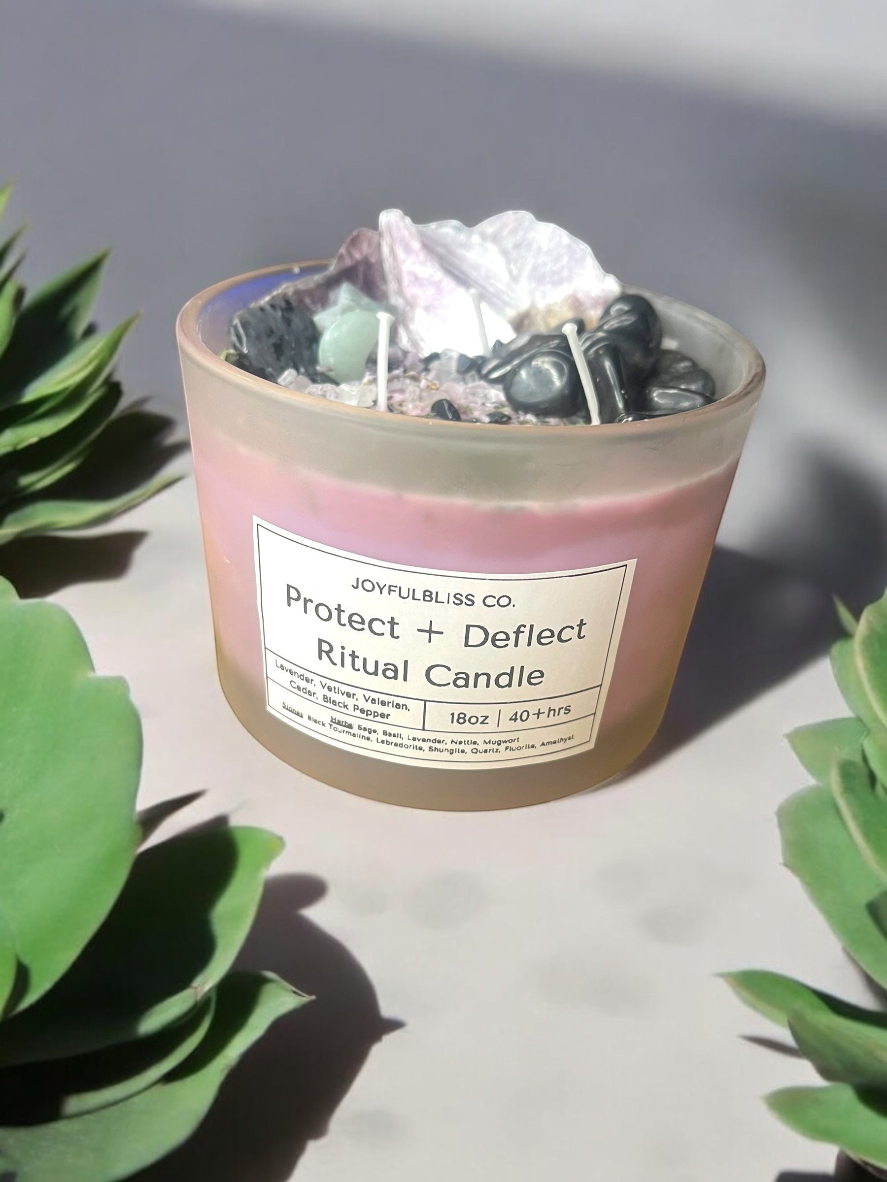 JoyfulBliss Co. Protect + Deflect soy ritual candle topped with crystals and herbs in a frosted glass jar.