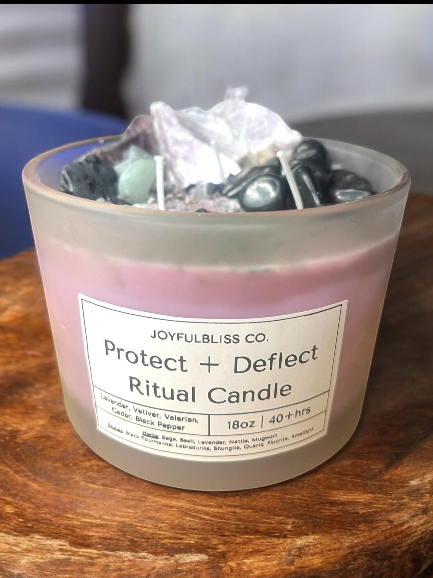 JoyfulBliss Co. Protect + Deflect ritual soy candle in a frosted glass jar topped with protective crystals.
