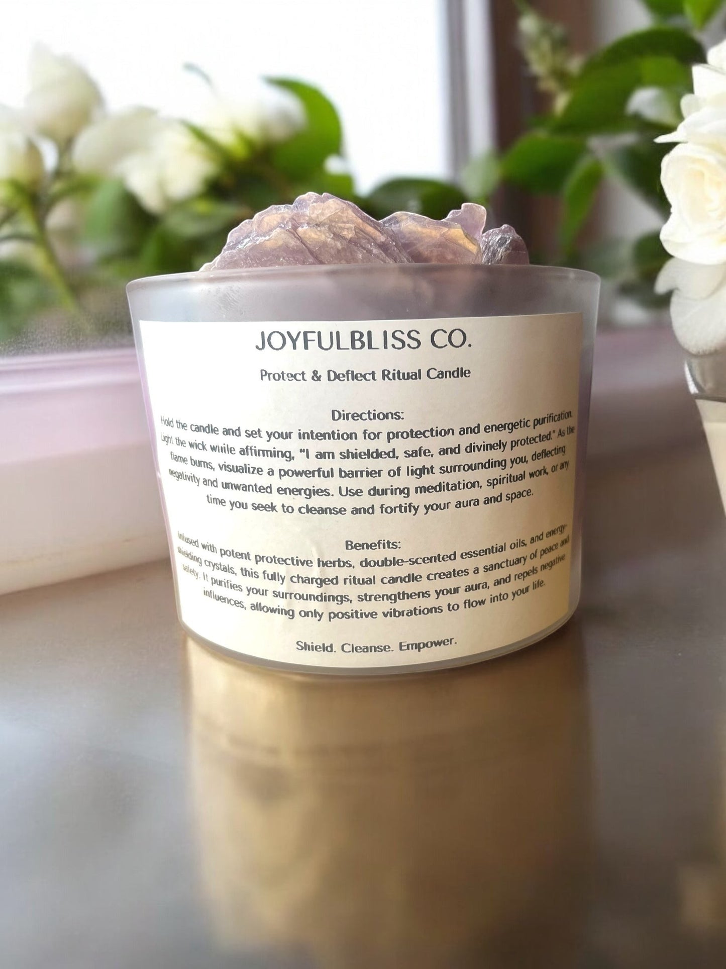 JoyfulBliss Co. Protect + Deflect soy ritual candle in a frosted glass jar topped with raw protective crystals.