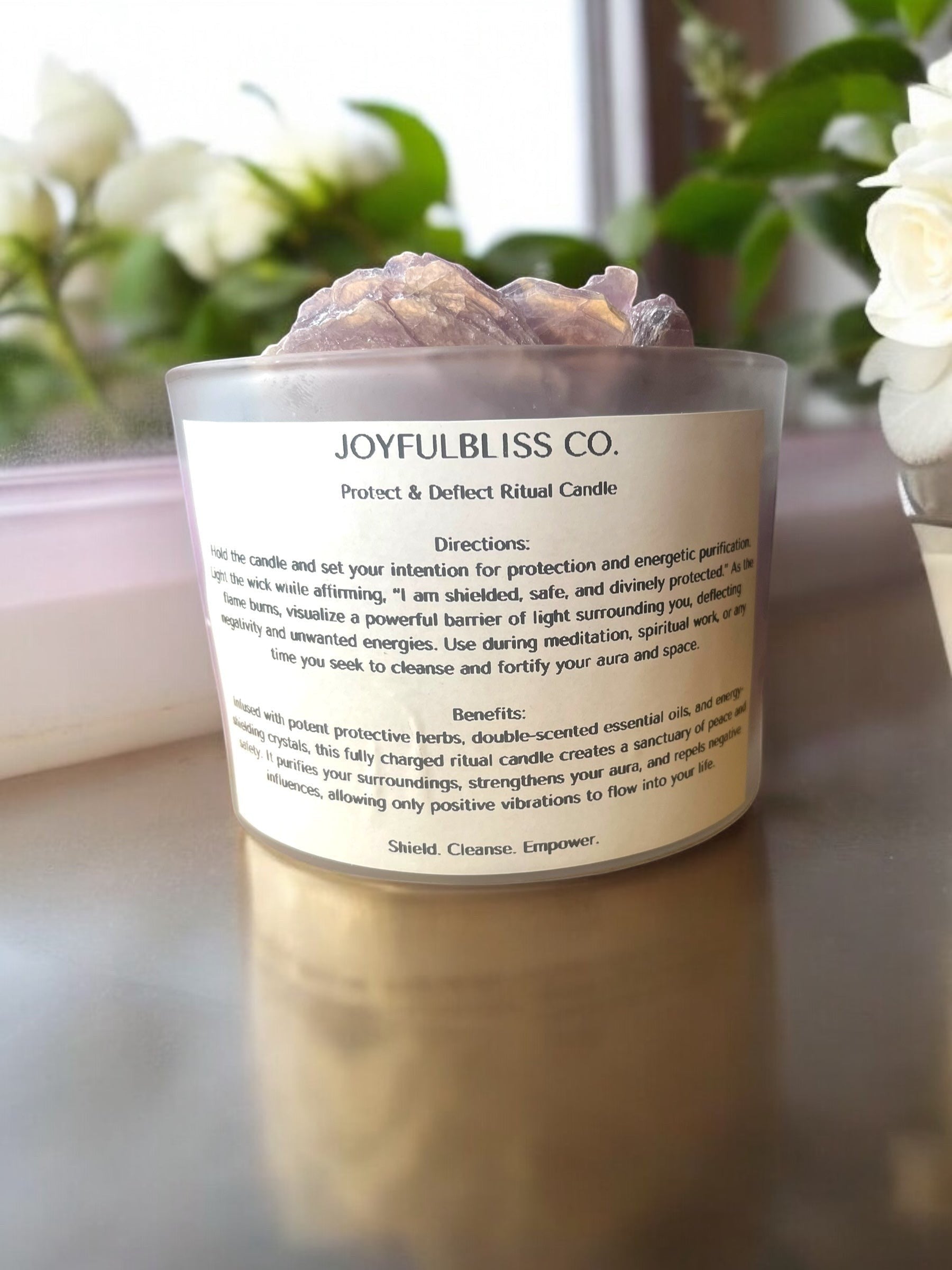 JoyfulBliss Co. Protect + Deflect soy ritual candle in a frosted glass jar topped with raw protective crystals.