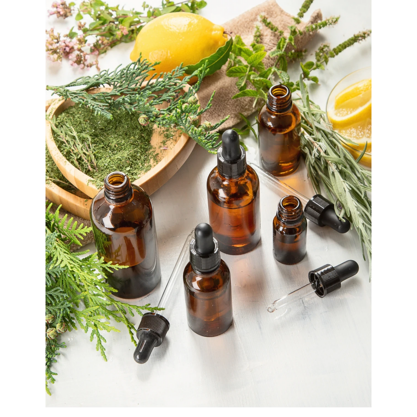 JoyfulBliss Co. ritual anointing oil in amber glass dropper bottles surrounded by fresh lemon, herbs, and greenery.