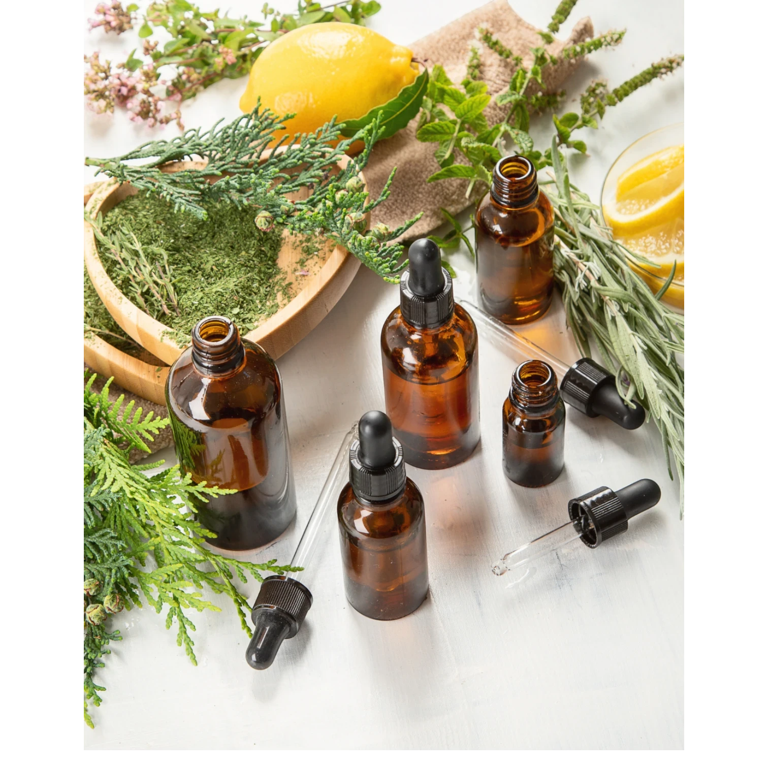 JoyfulBliss Co. ritual anointing oil in amber glass dropper bottles surrounded by fresh lemon, herbs, and greenery.