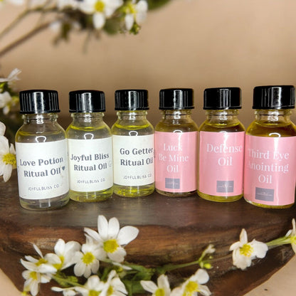 JoyfulBliss Co. collection of ritual anointing oils in small glass bottles with white and pink labels on wood surface