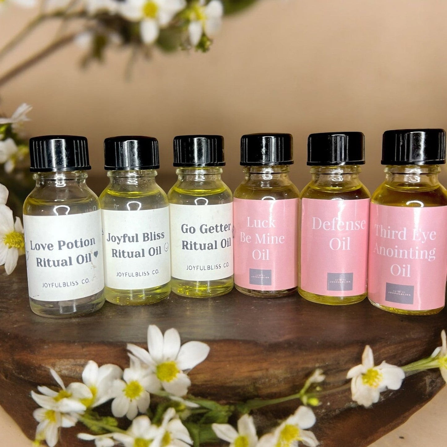JoyfulBliss Co. collection of ritual anointing oils in small glass bottles with white and pink labels on wood