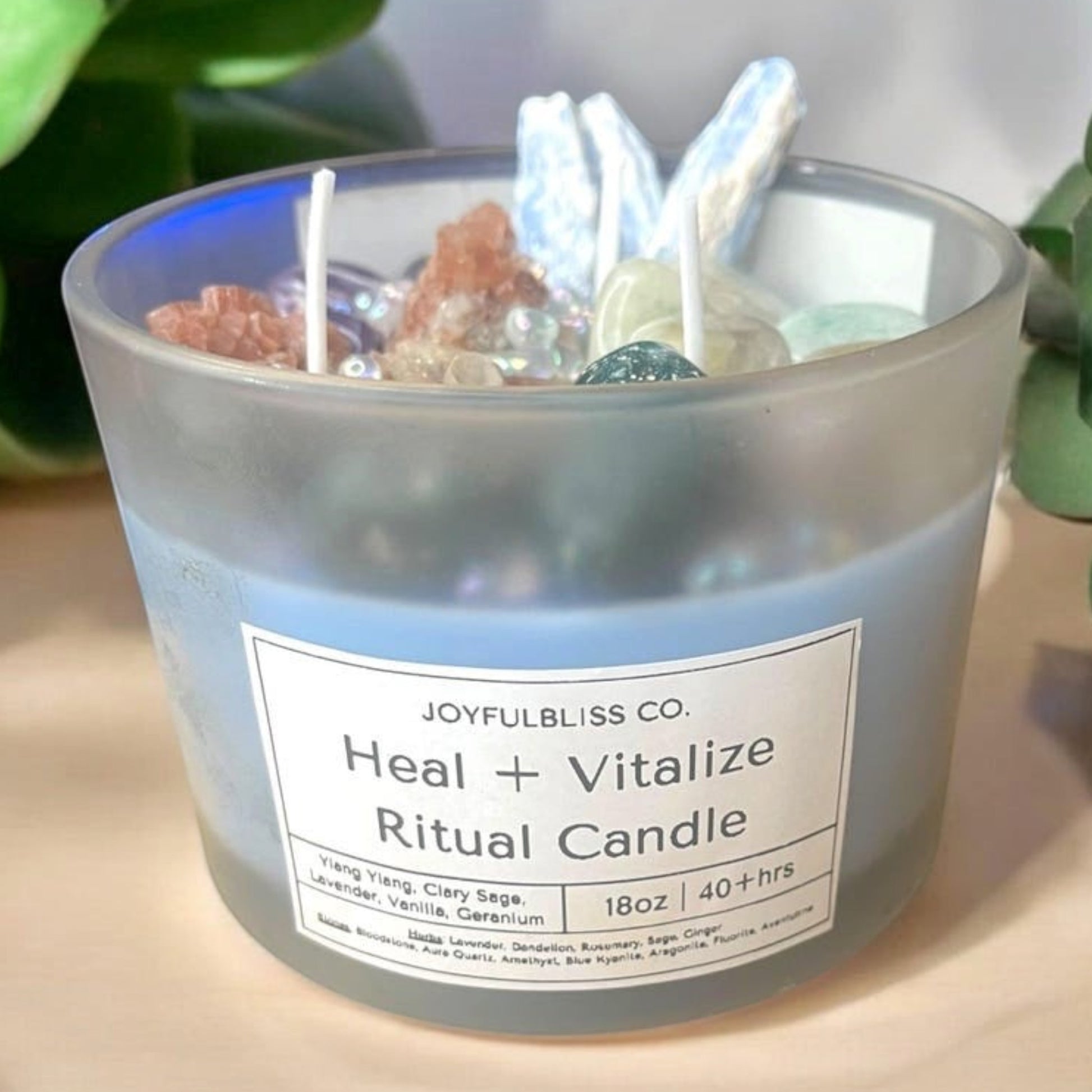 JoyfulBliss Co. Heal + Vitalize ritual candle in a frosted glass jar topped with healing crystals and herbs