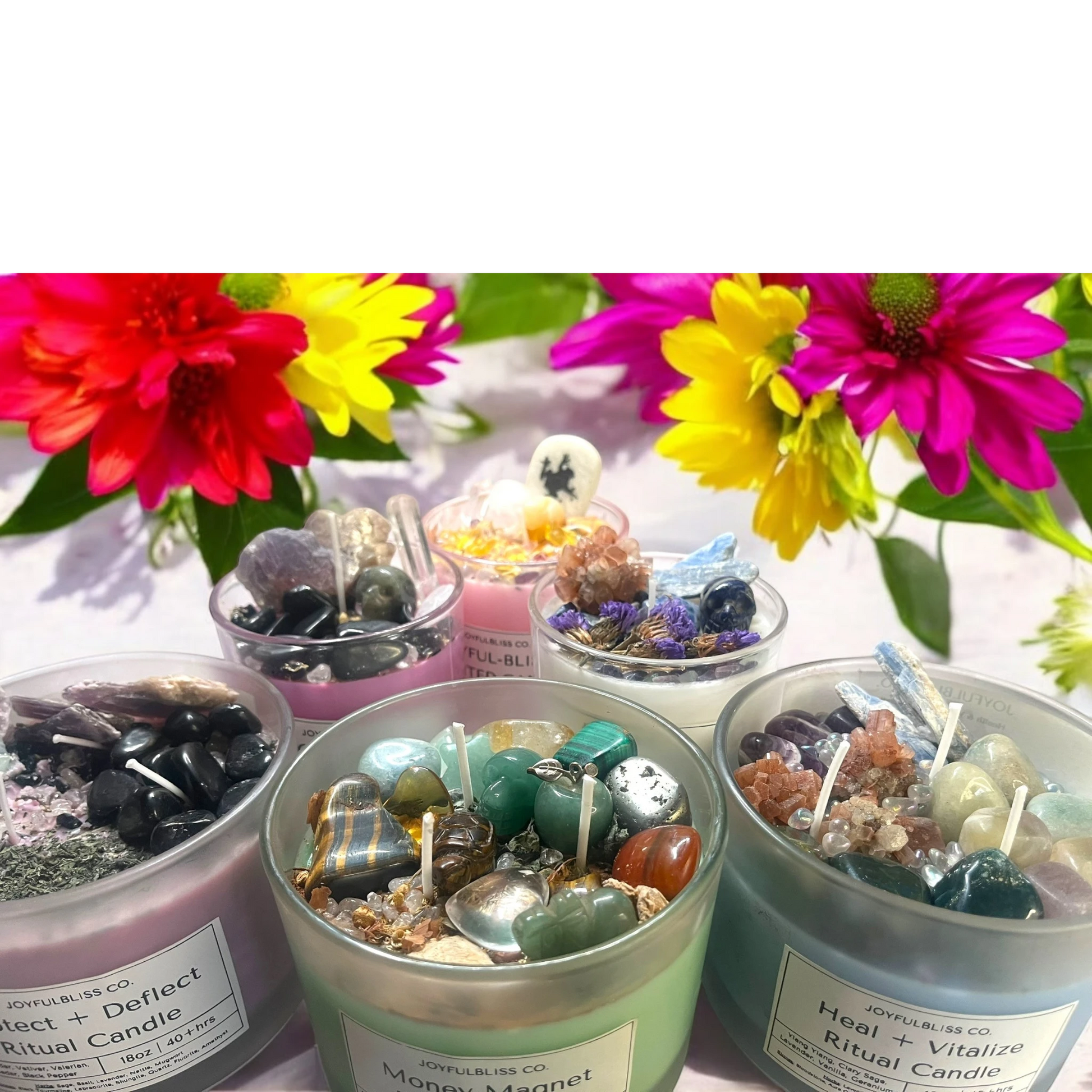 JoyfulBliss Co. ritual candles topped with healing crystals and herbs, displayed with vibrant flowers for energy renewal.