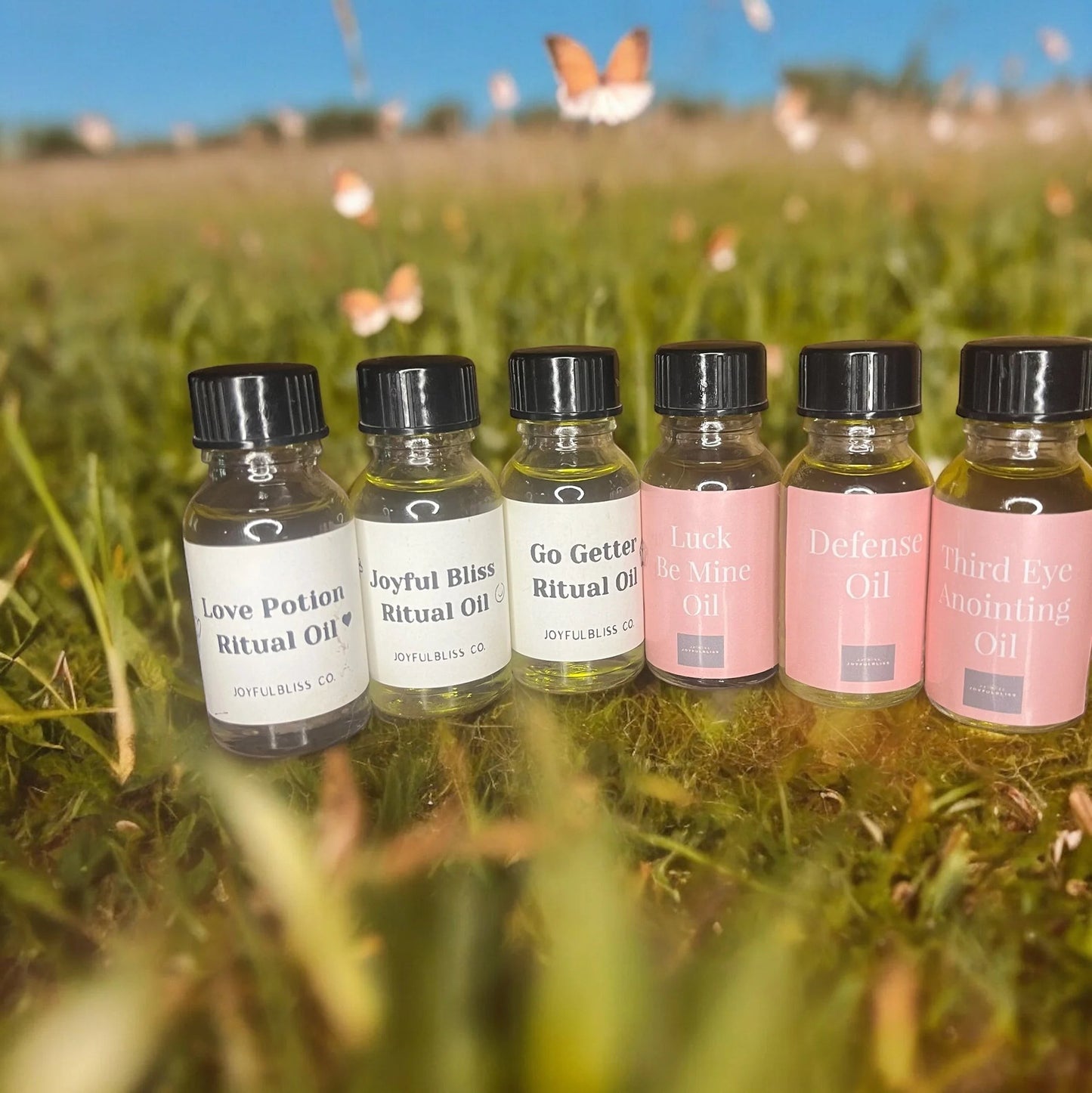 JoyfulBliss Co. ritual oil collection set of six handcrafted botanical essential oils in a sunny outdoor field.
